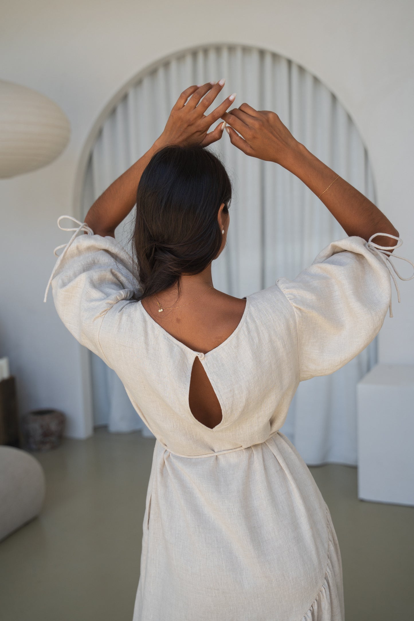 LILLY PILLY woman in an oatmeal Charlotte linen dress back view close up while standing in a minimalistic room