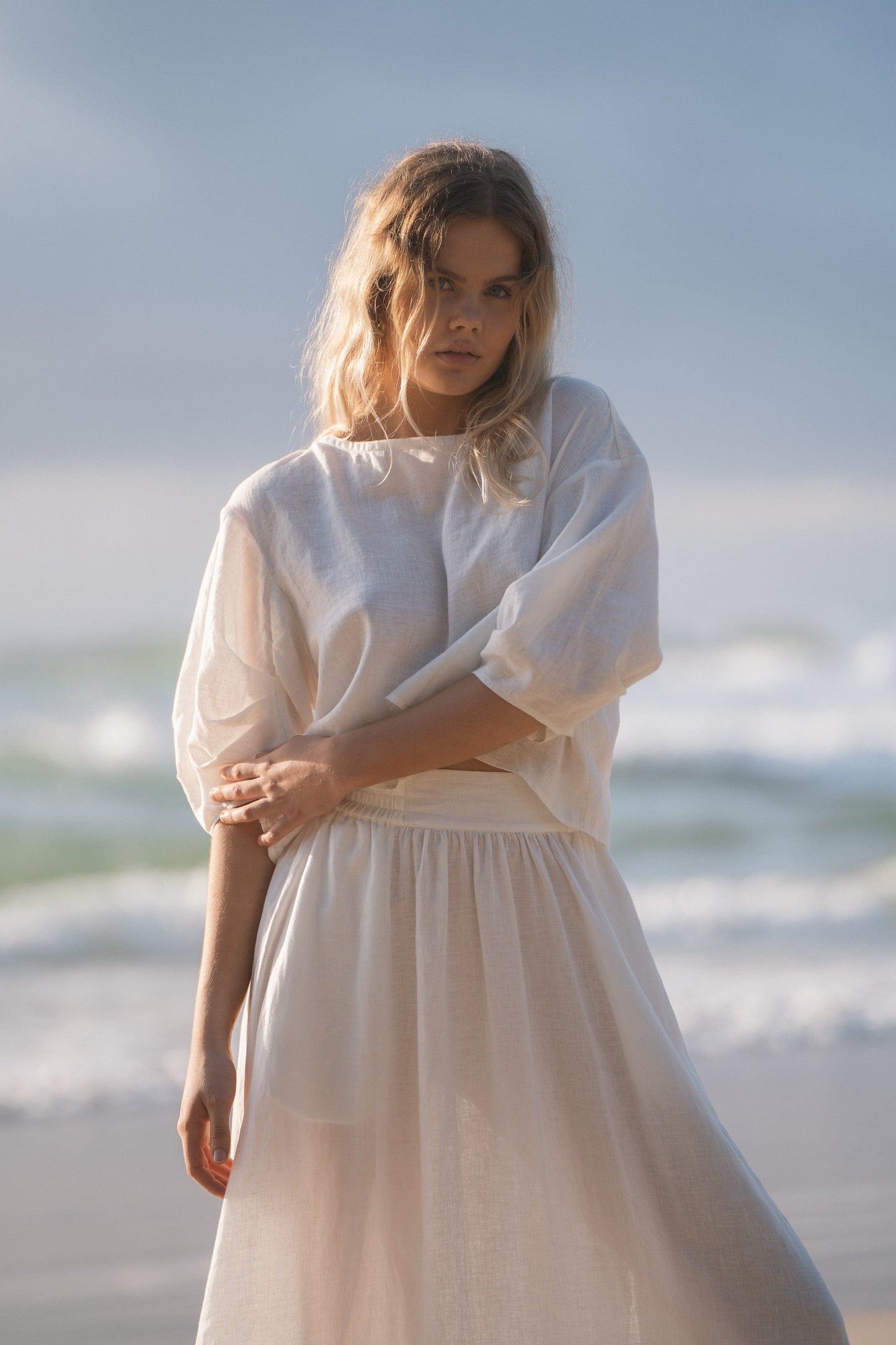 Lilly Pilly Collection Hannah skirt made from European linen in Ivory with Tina linen top in Ivory standing in front of the water