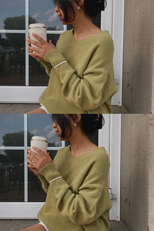 LILLY PILLY woman in an a olive green, June Cashmere knit, sweater holding a coffee cup in front of a glass door.