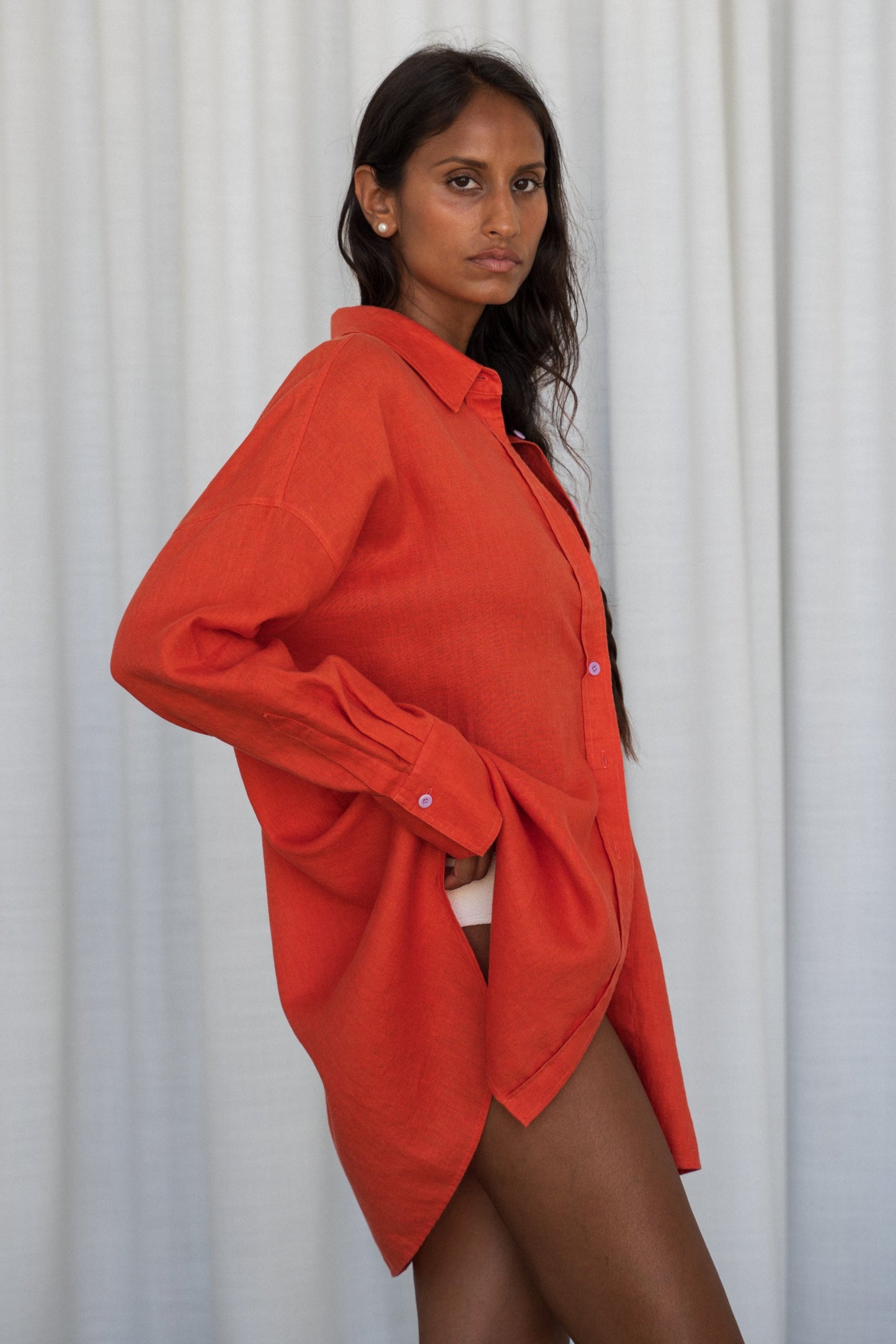 LILLY PILLY woman wearing a spritz Kirra linen shirt leaning against a white curtain background